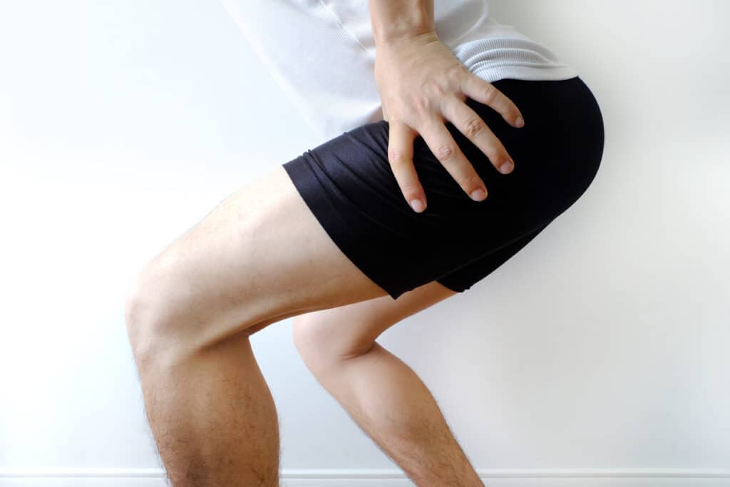 Man crouched and holding his hip in pain, likely in need of either hip resurfacing or total hip replacement surgery