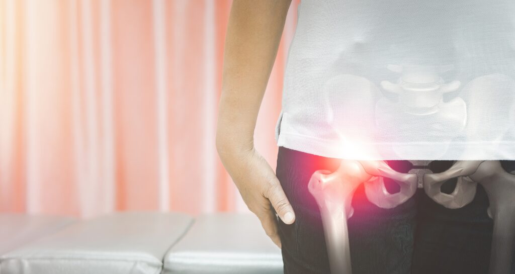 Person holding hip in pain, with medical illustration of hip bones and highlighted joint area showing discomfort, representing avascular necrosis or hip joint problems