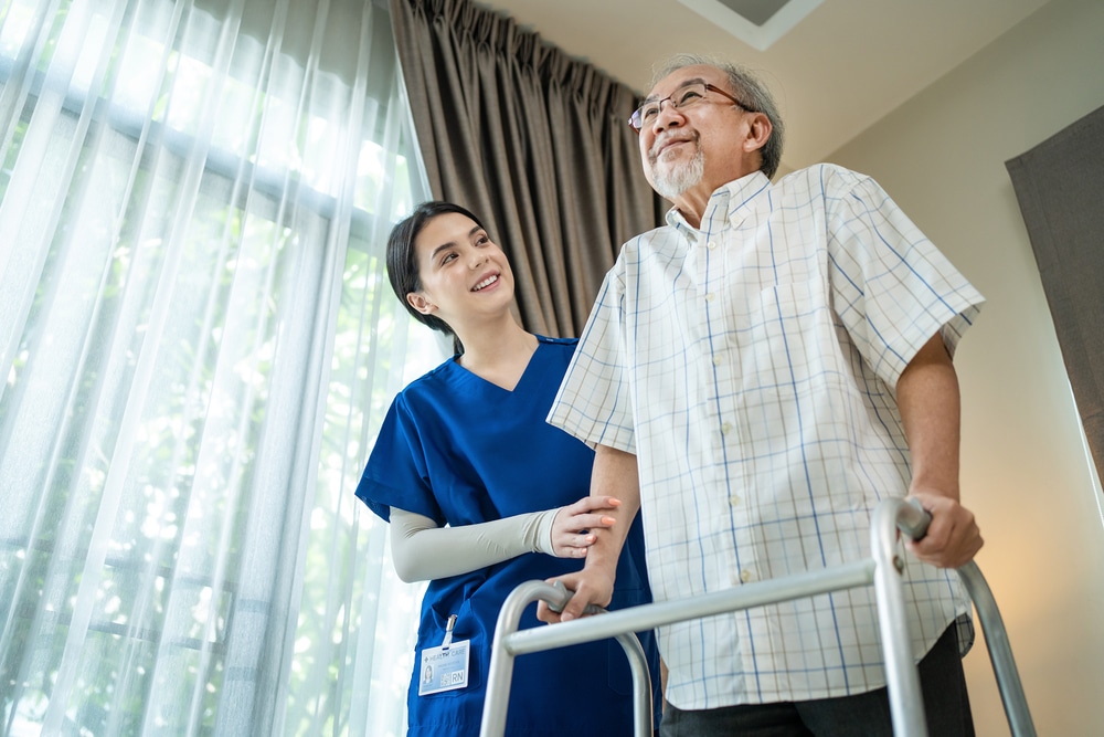 Elderly man using walker in home after hip surgery with assistance of nurse.
